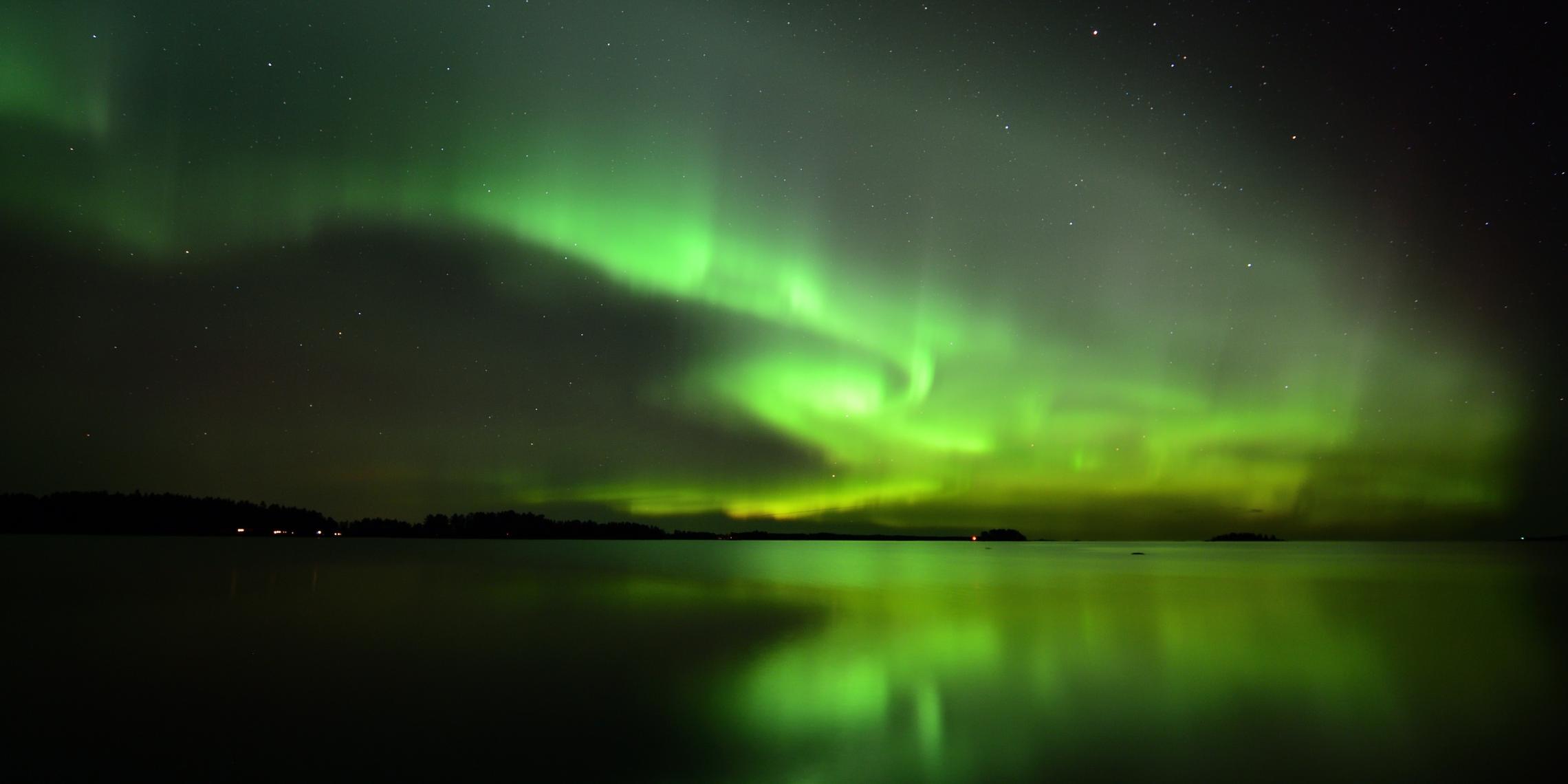 Hier sieht man Polarlicht über demWasser, im Hintergrund eine Küstenstadt